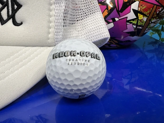 A golf ball with a printed logo for Neon Opal Creative Studios on a blue surface - Custom golf balls for corporate event favors — Oklahoma City